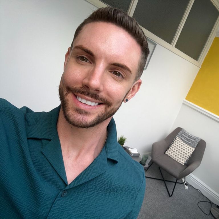 Jamie Moffat, an integrative therapist, is smiling in a welcoming therapy room setting in Manchester.