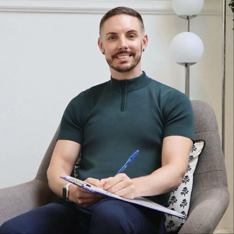 Jamie Moffat, an integrative therapist, is smiling in a welcoming therapy room setting in Manchester.