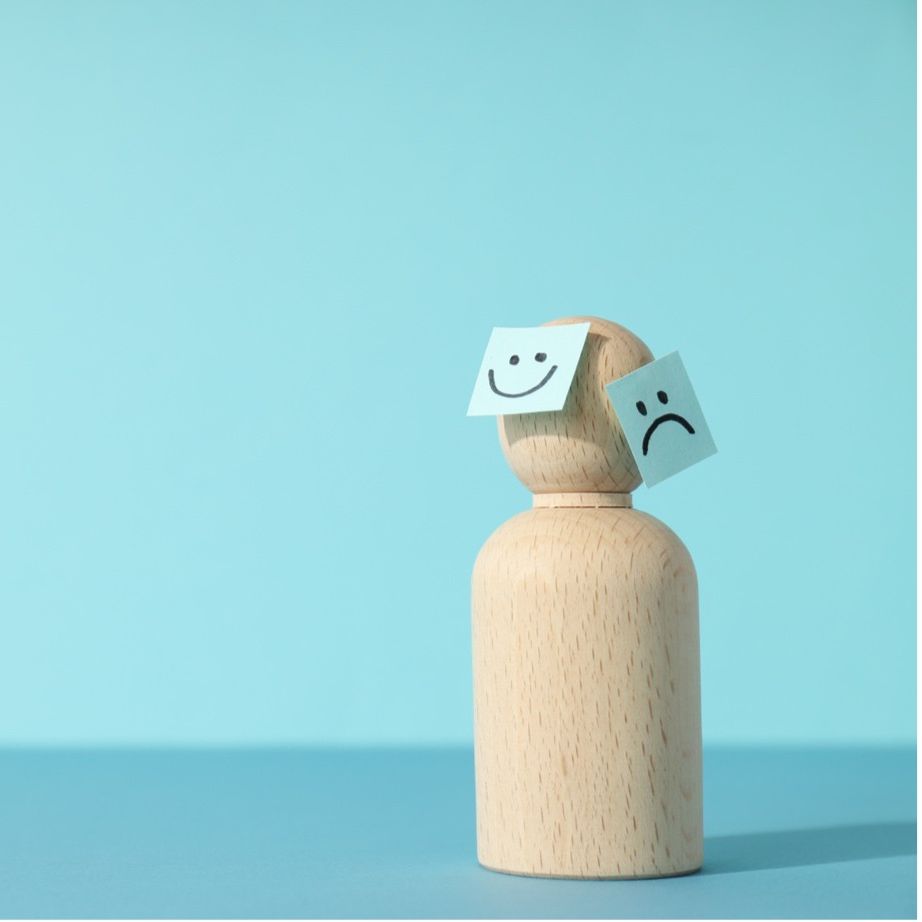 A wooden figure with happy and sad face stickers, representing people-pleasing, anxiety, and walking on eggshells in Manchester.